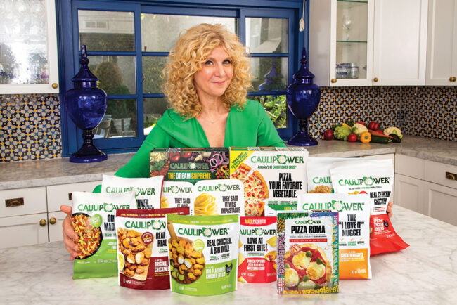 A smiling woman with curly blond hair displays several frozen cauliflower products