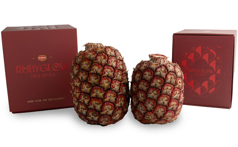 A ruby red pineapple pictured with the dark red box it's soldin