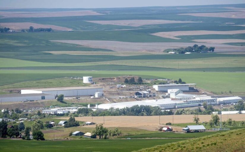 An aerial shot of a food production facility with green hills and farmland in the background