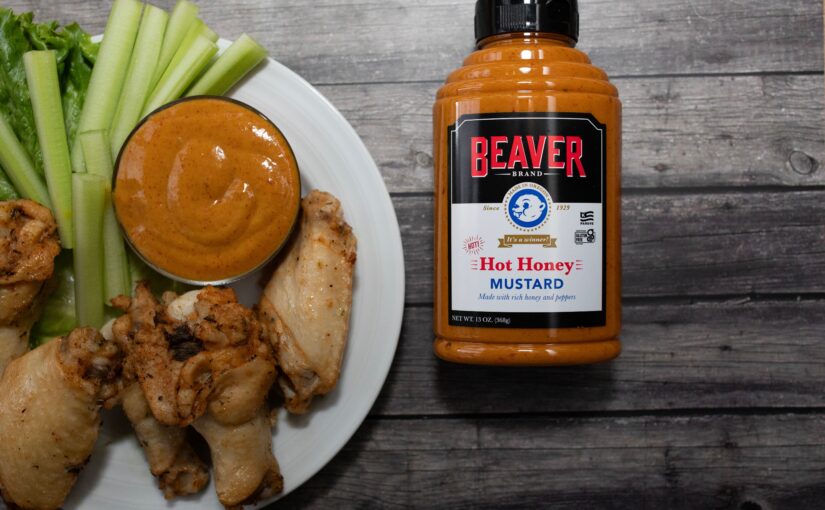 A jar of spicy mustard next to a plate of wings and celery