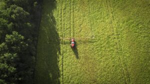 An overhead view of a red tractor on a vast, green field