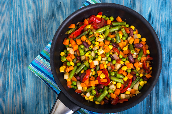 A pan of freshly sauteed vegetables including carrots, corn and snap peas