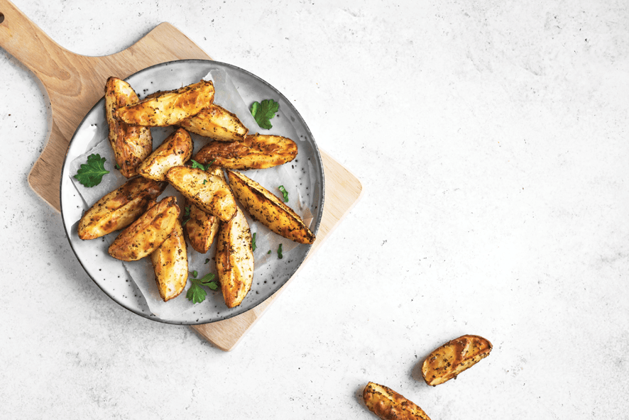 Freshly seasoned potato wedges garnished with parsley on a white plate