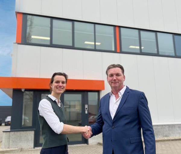 A woman and a man in business attire shake hands in front of an office building