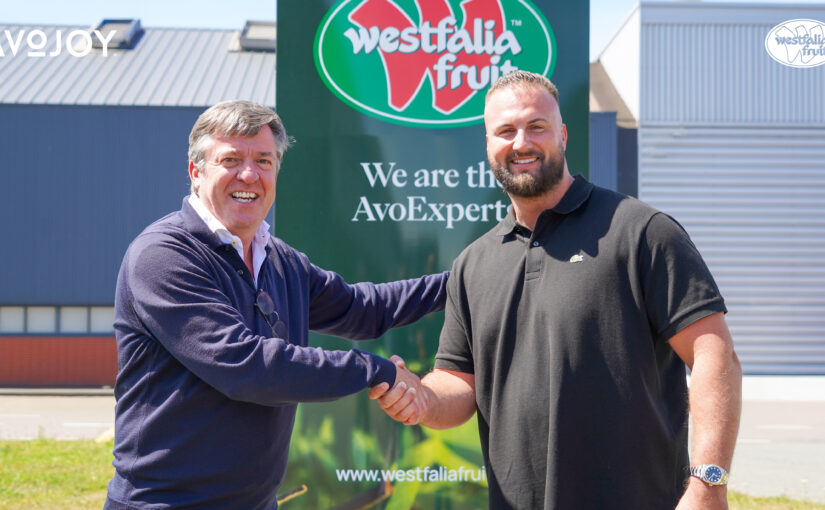 Two men shake hands in front of the red-and-green Westfalia Fruit logo